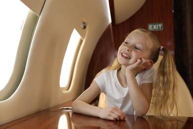 Photo of Cute little girl looking out window at table in airplane during flight
