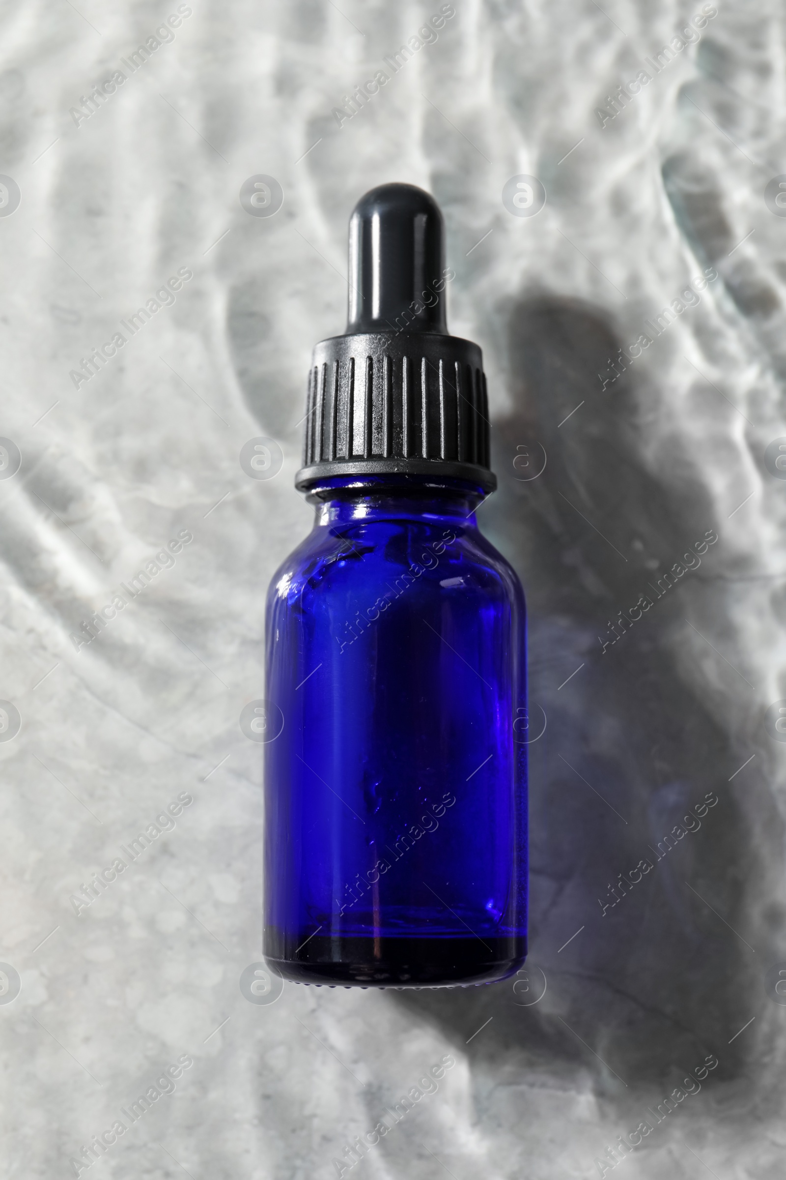 Photo of Bottle of face serum in water on light background, top view