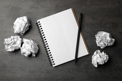 Photo of Empty notebook with pencil and crumpled paper balls on grey table, flat lay. Space for text