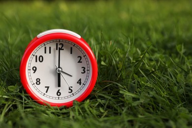 Photo of Red alarm clock on green grass outdoors, space for text