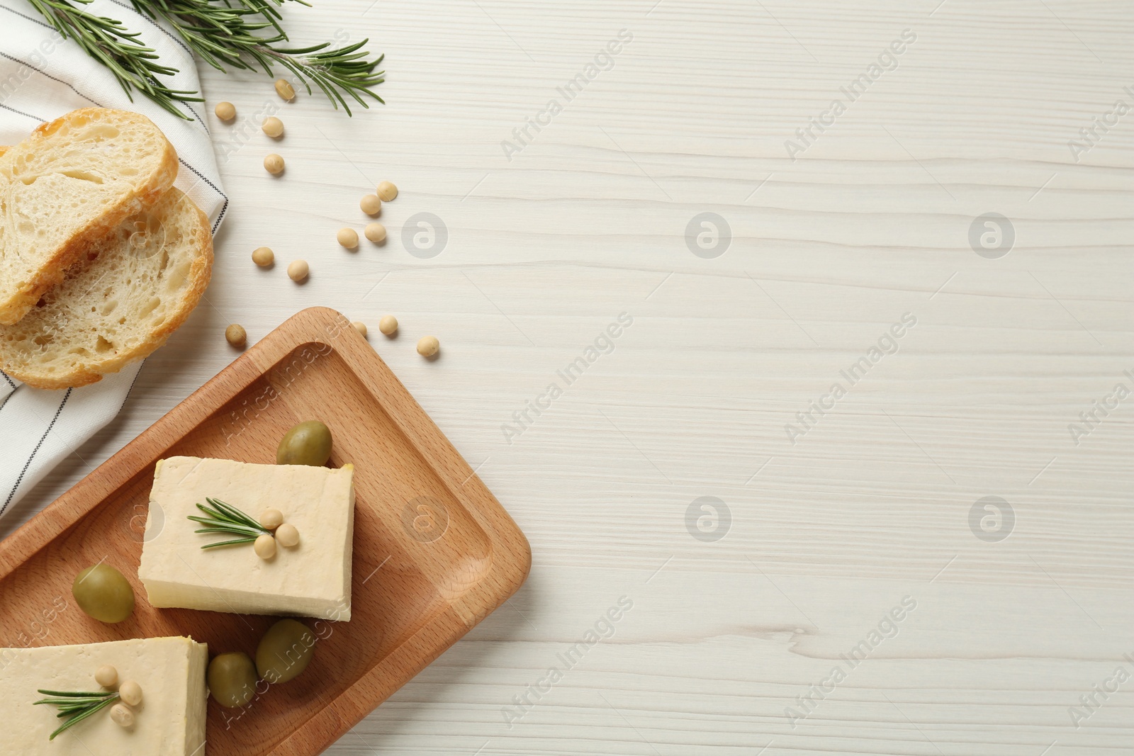 Photo of Pieces of delicious tofu with rosemary, olives and soy on white wooden table, flat lay. Space for text