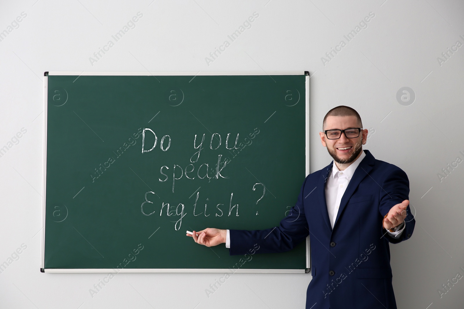 Photo of Teacher near green chalkboard with words Do You Speak English?