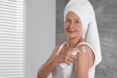Photo of Happy woman applying body cream onto shoulder indoors. Space for text