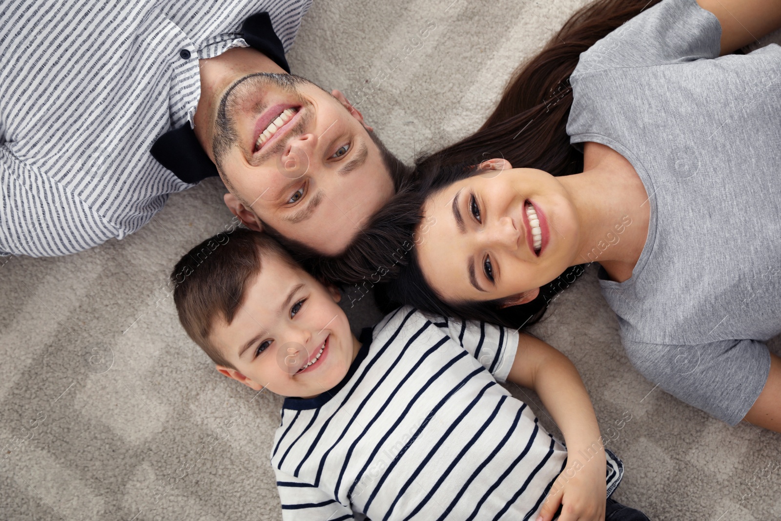 Photo of Happy parents and their son lying together on floor, view from above. Family time