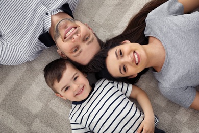 Happy parents and their son lying together on floor, view from above. Family time