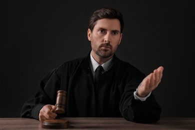 Photo of Judge with gavel sitting at wooden table against black background