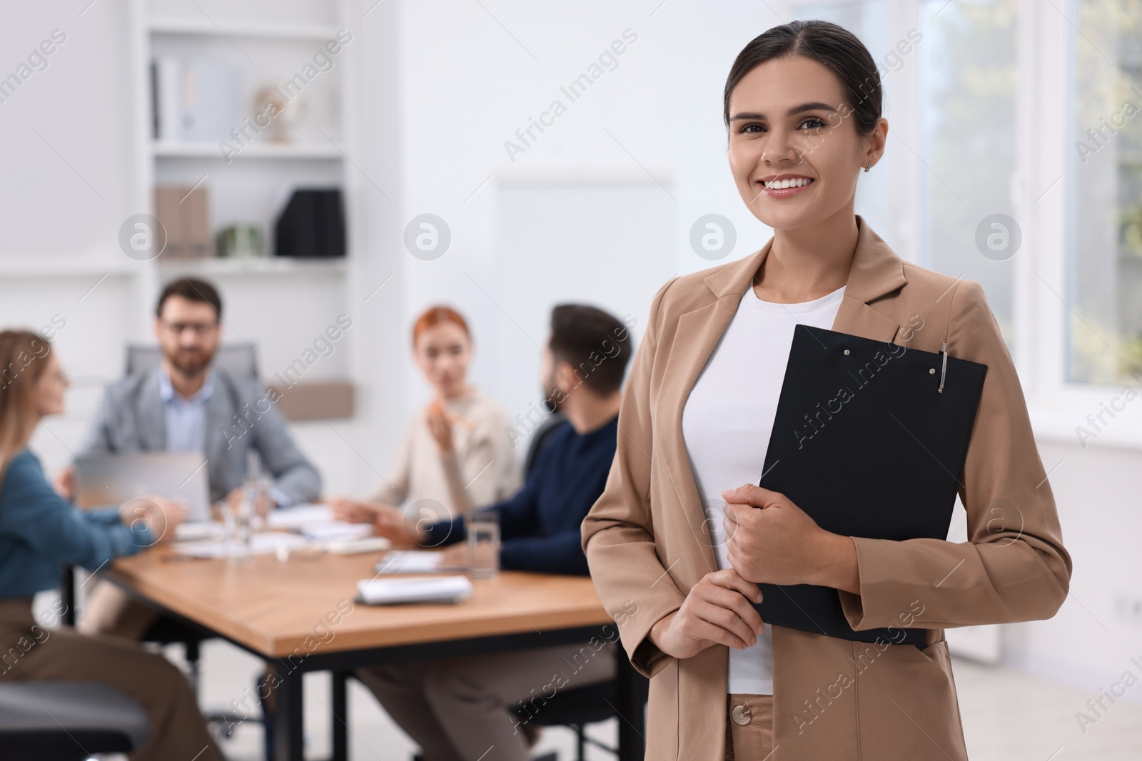 Photo of Team of employees working together in office. Happy woman with clipboard indoors