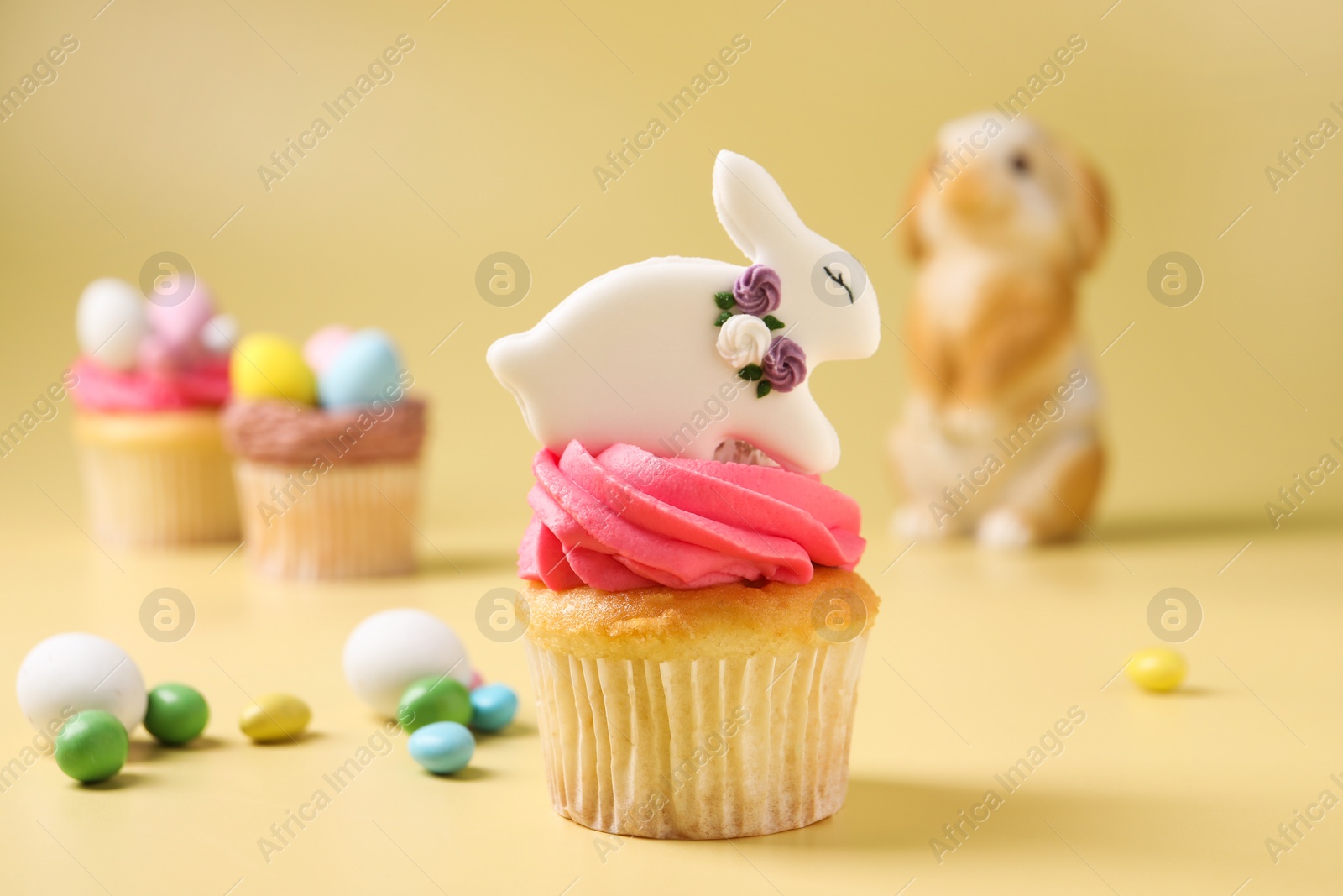 Photo of Tasty cupcakes with Easter decor on pale yellow background, closeup