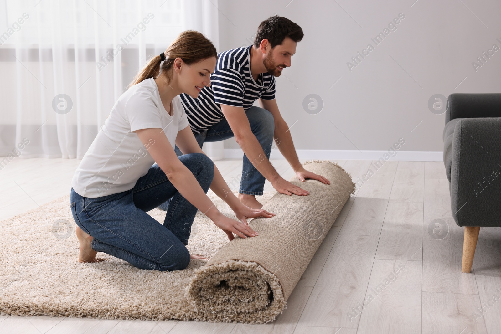 Photo of Smiling couple unrolling carpet on floor in room