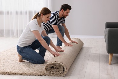 Smiling couple unrolling carpet on floor in room