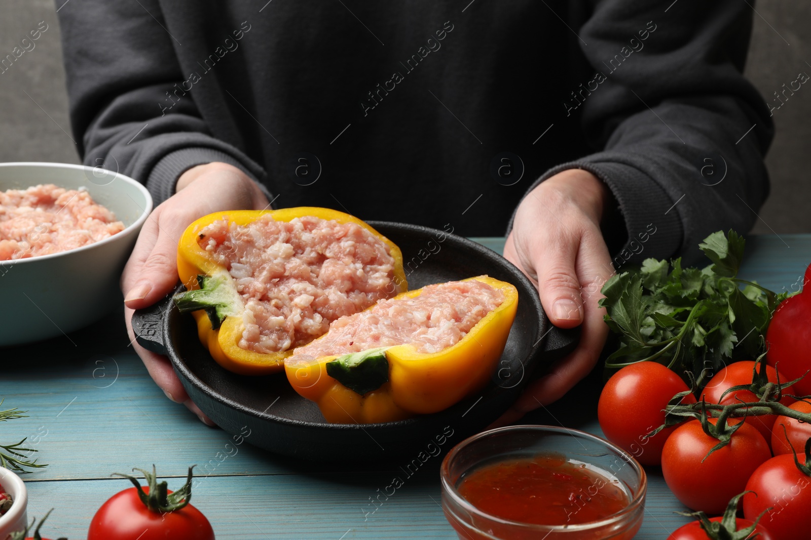 Photo of Woman making stuffed peppers with ground meat at light blue wooden table, closeup