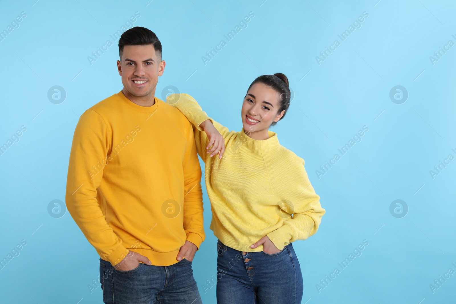 Photo of Happy couple wearing yellow warm sweaters on light blue background. Space for text