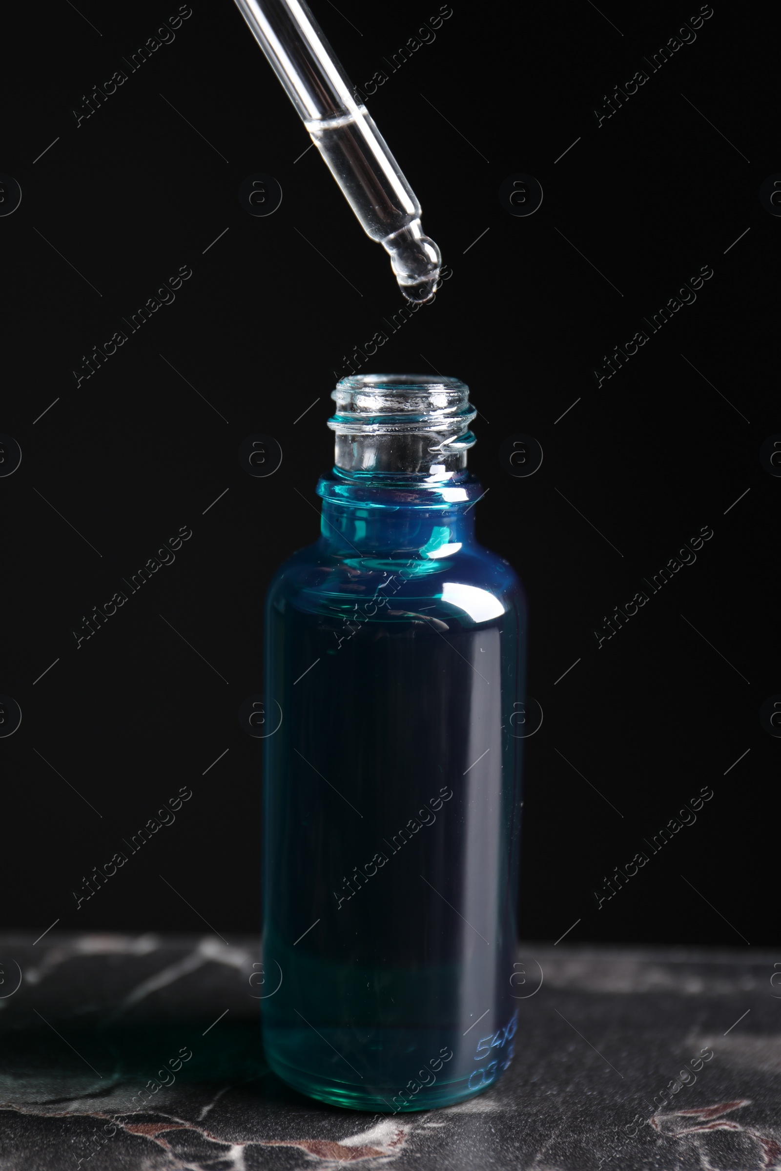 Photo of Dripping cosmetic serum from pipette into bottle on grey marble table