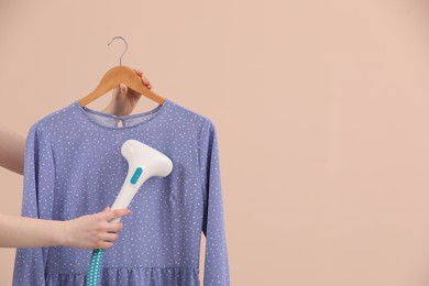 Woman steaming blouse on hanger against beige background, closeup. Space for text