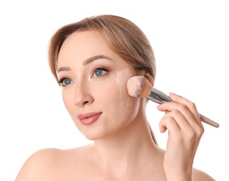 Beautiful young woman applying face powder with brush on white background