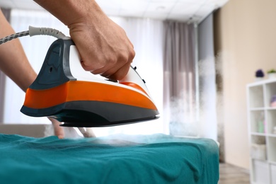 Man ironing clothes on board at home, closeup