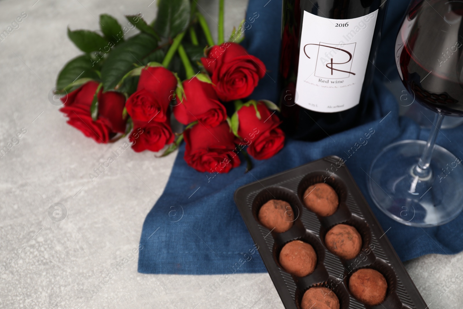 Photo of Red wine, chocolate truffles and roses on light textured table, closeup