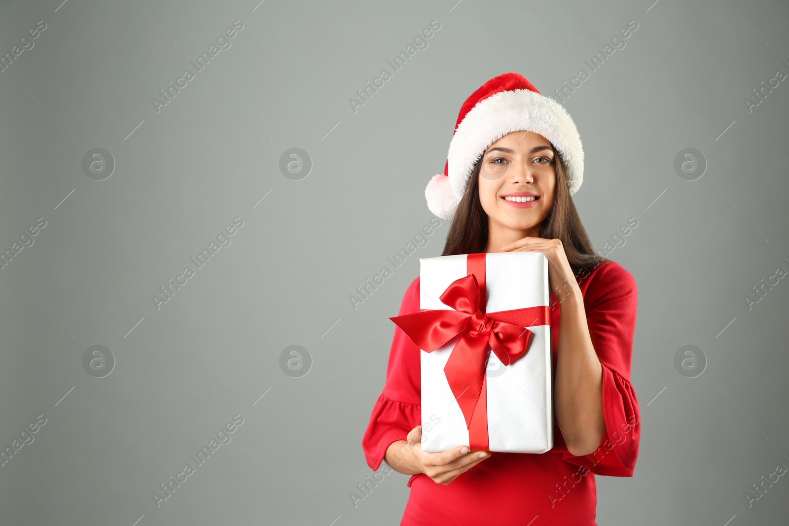 Photo of Young beautiful woman in Santa hat with gift box on grey background. Christmas celebration