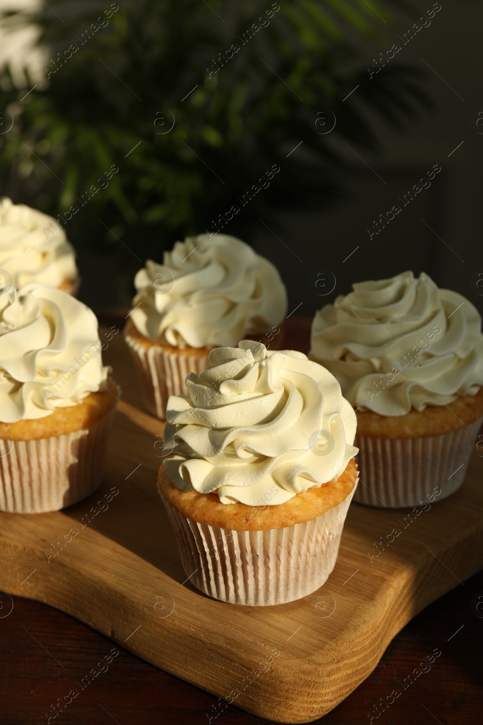 Photo of Tasty cupcakes with vanilla cream on wooden table, closeup