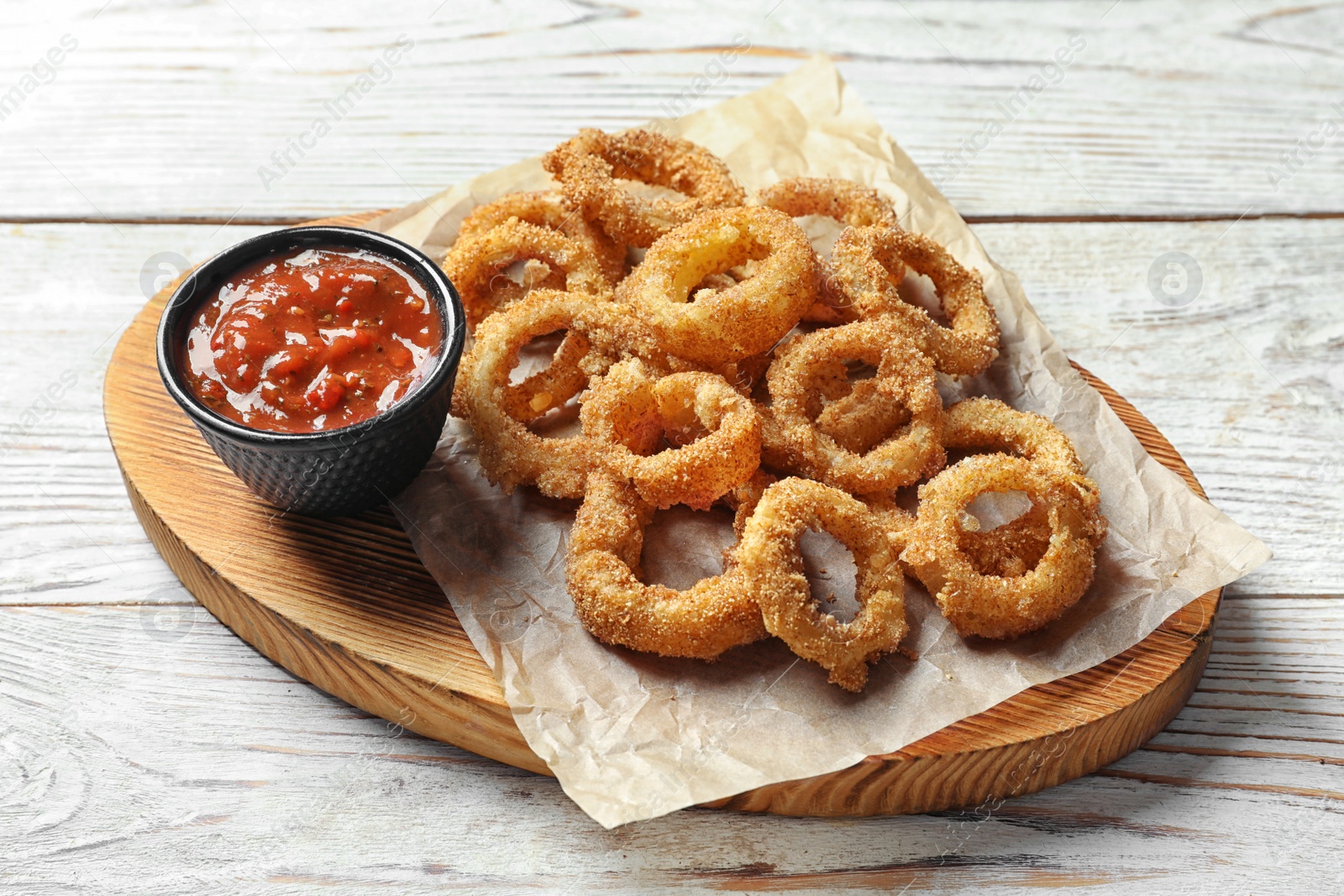 Photo of Homemade crunchy fried onion rings with tomato sauce on wooden table