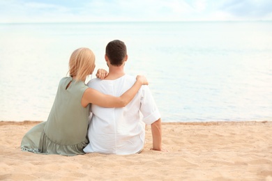 Photo of Happy romantic couple sitting together on beach, space for text
