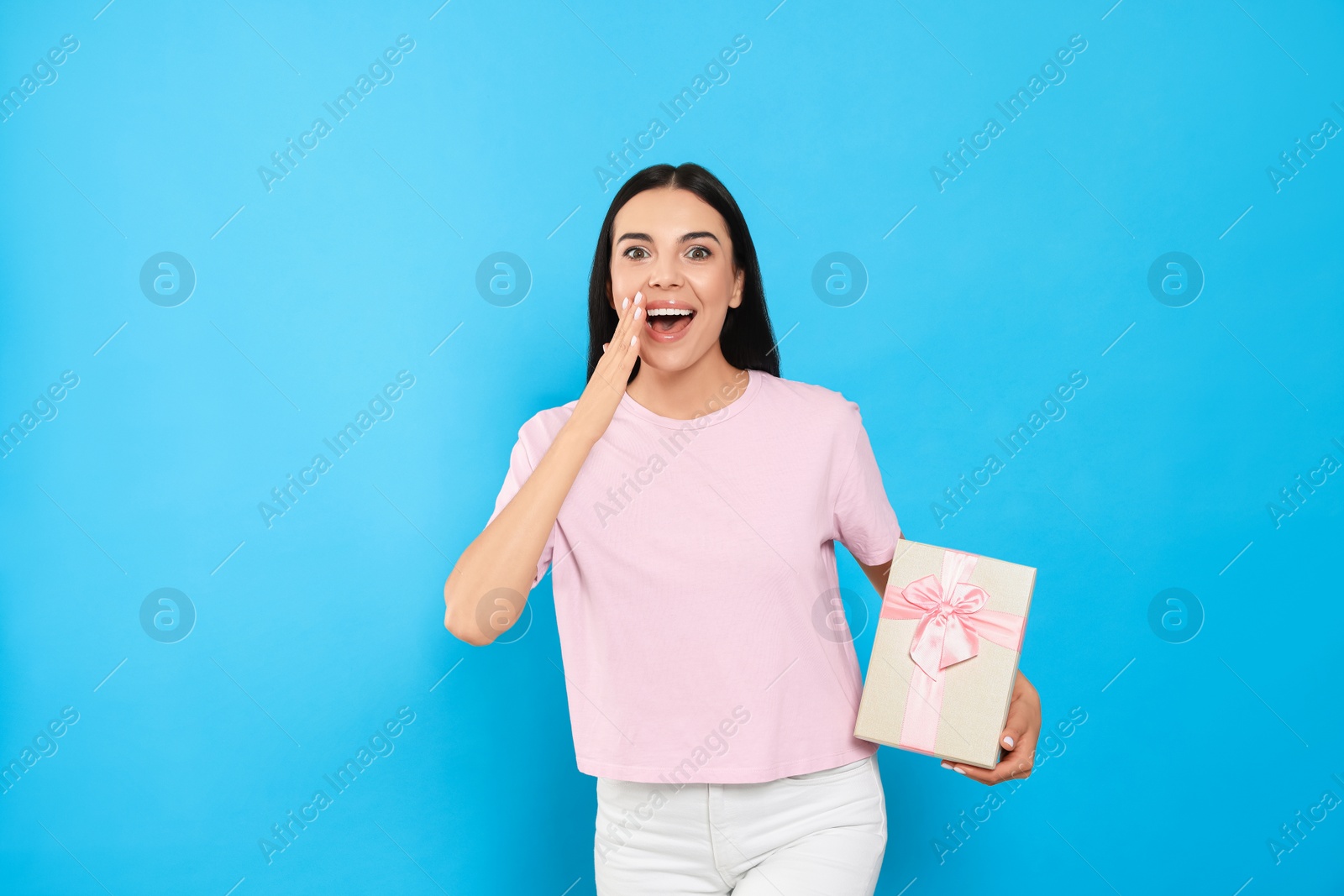 Photo of Emotional young woman holding gift box on light blue background