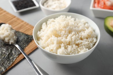 Cooked rice in bowl for sushi on grey textured table, closeup