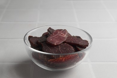 Bowl with pieces of delicious beef jerky on white tiled table