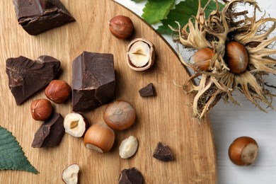 Delicious chocolate chunks and hazelnuts on white wooden table, flat lay