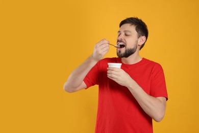 Photo of Handsome man eating tasty yogurt on orange background