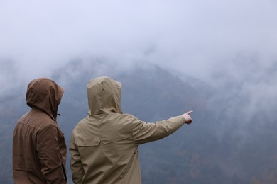 Photo of Man and woman in raincoats enjoying mountain landscape