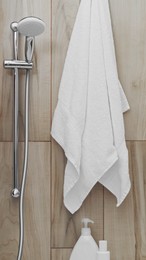 Photo of White soft towel near showerhead on tiled wall in bathroom