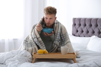 Sick young man eating soup to cure flu in bed at home