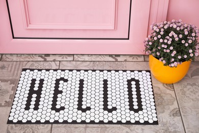 Photo of Stylish door mat with word HELLO and beautiful flowers near entrance