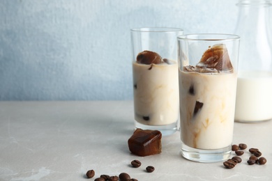 Photo of Glasses of milk with coffee ice cubes and beans on table against color background. Space for text