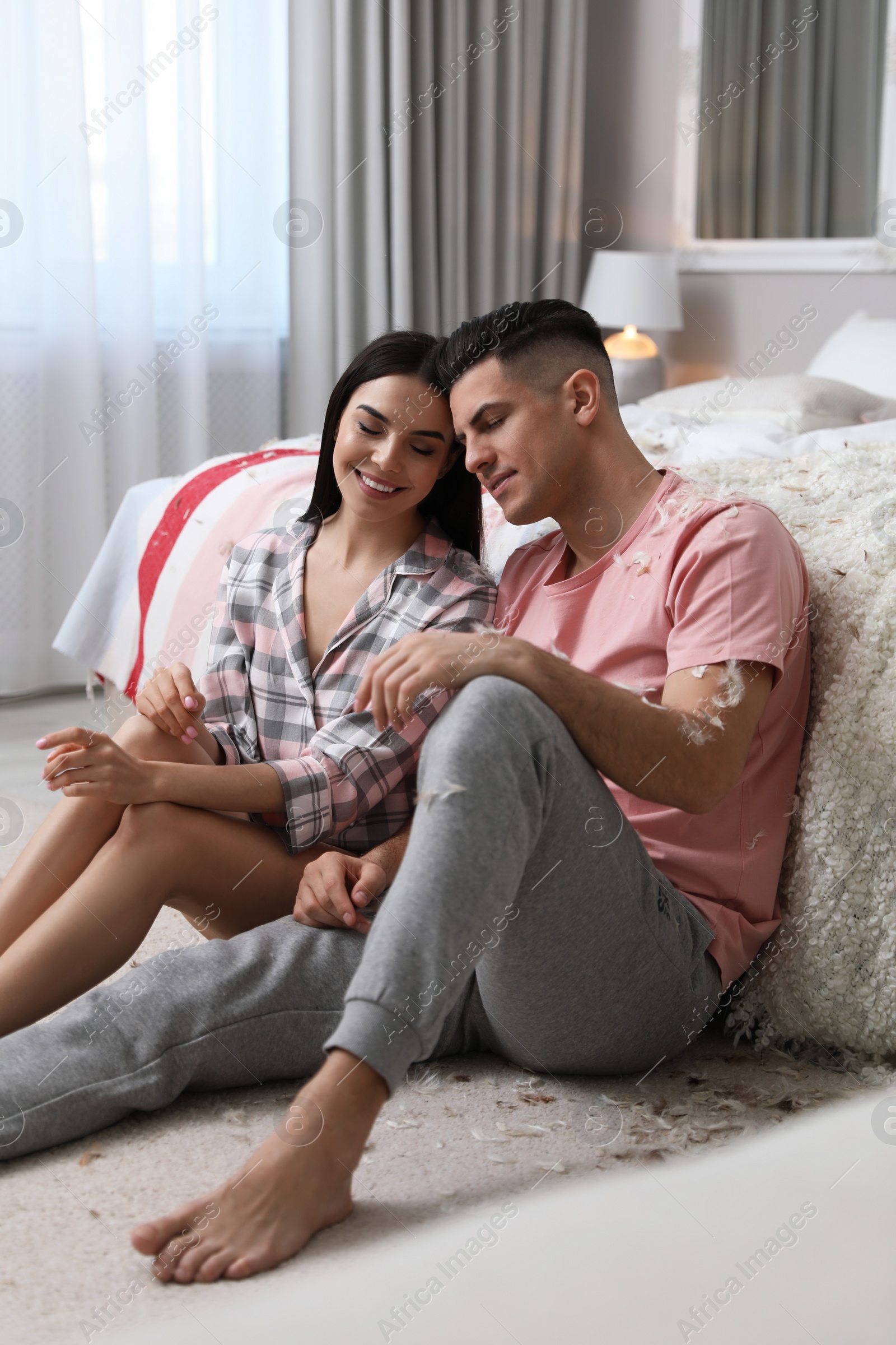 Photo of Happy couple resting on floor near bed after pillow fight