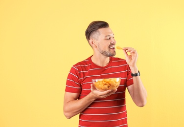 Man eating potato chips on color background