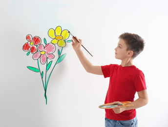 Image of Little boy drawing flowers on white wall 