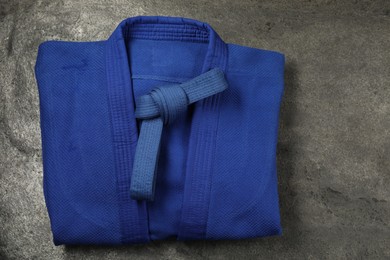 Photo of Blue karate belt and kimono on gray textured background, top view