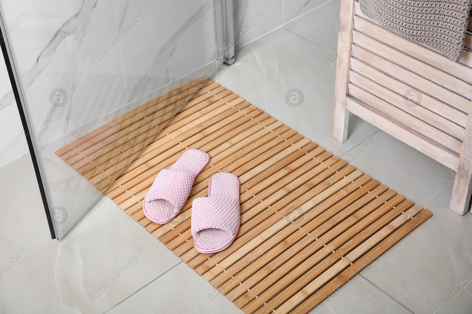 Photo of Wooden mat with slippers on floor in bathroom