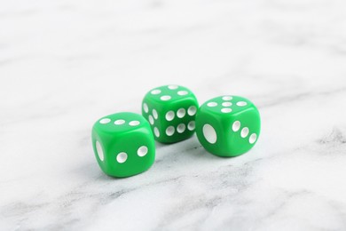 Photo of Three green game dices on white marble table, closeup