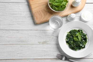 Photo of Flat lay composition with tasty cooked spinach and space for text on white wooden table. Healthy food