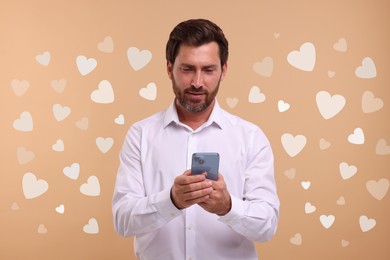 Image of Long distance love. Man chatting with sweetheart via smartphone on dark beige background. Hearts around him
