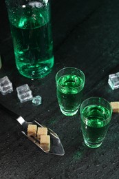 Absinthe in shot glasses, spoon, brown sugar and ice cubes on gray table. Alcoholic drink