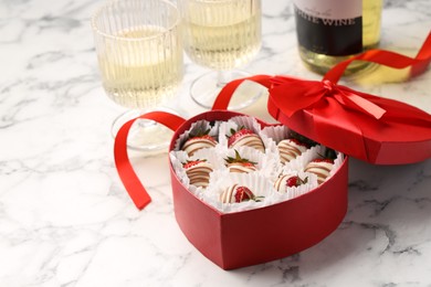 Delicious chocolate covered strawberries in heart shaped box and sparkling wine on white marble table. Space for text