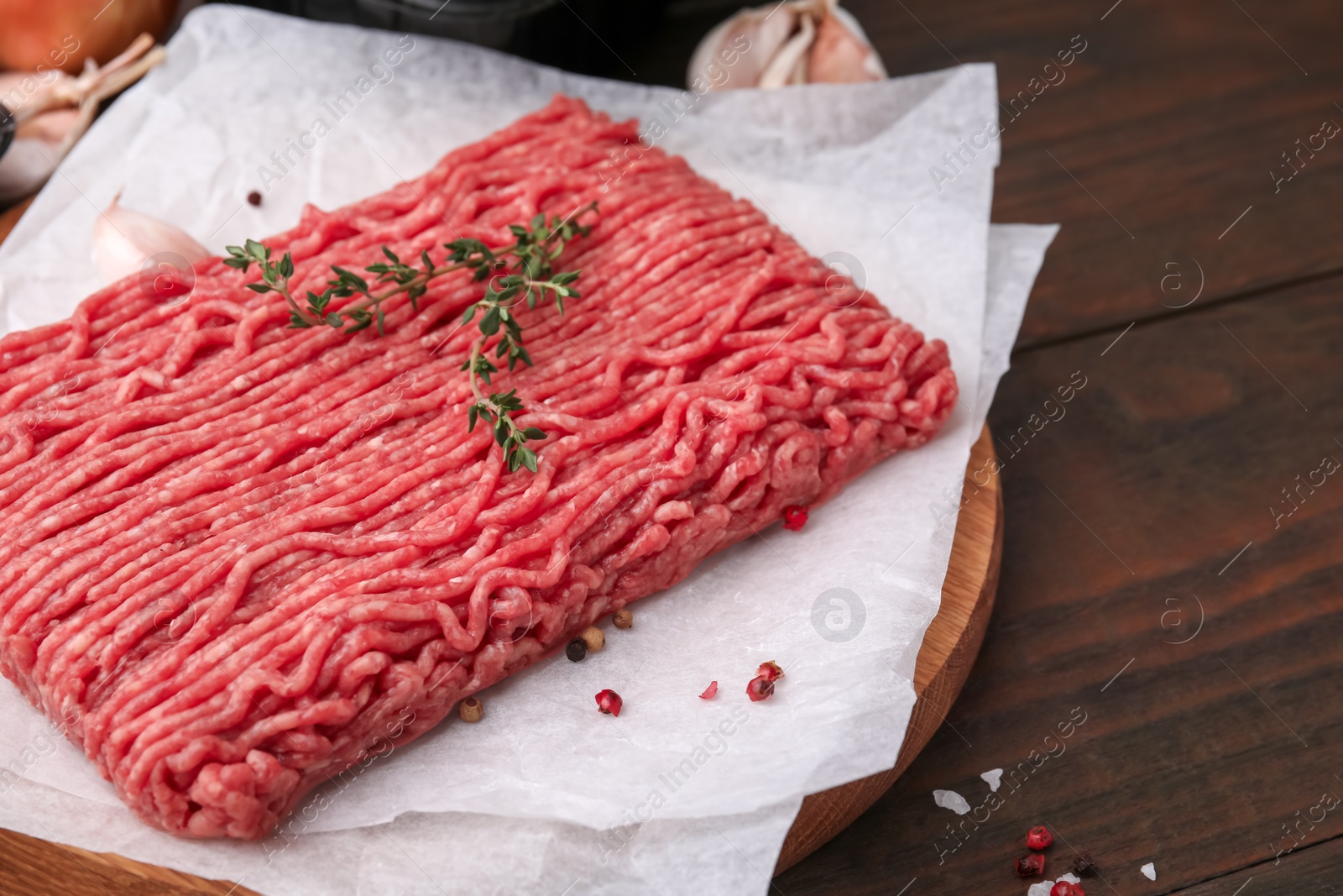 Photo of Fresh raw ground meat, thyme and peppercorns on wooden table, closeup