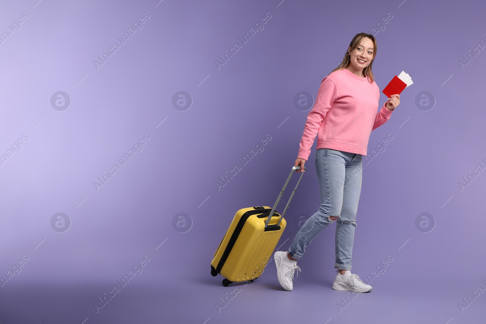 Photo of Happy young woman with passport, ticket and suitcase on purple background, space for text