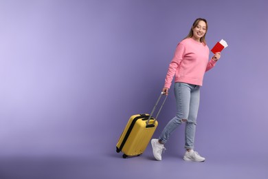 Photo of Happy young woman with passport, ticket and suitcase on purple background, space for text