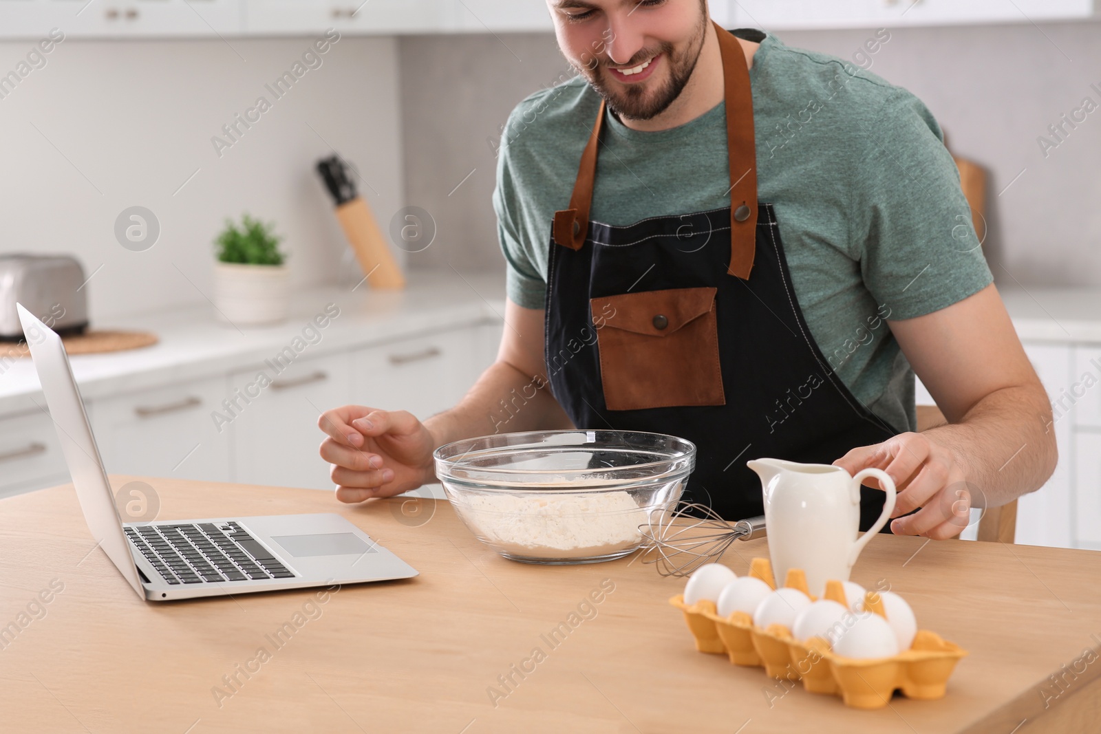 Photo of Man learning to cook with online video at wooden table in kitchen, closeup. Time for hobby