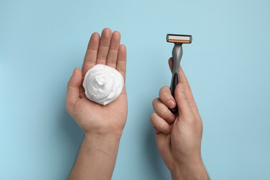 Photo of Man holding shaving foam and razor on light blue background, top view